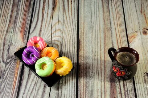 A rectangular black plate with several donuts in multi-colored glaze and a mu Stock Photos