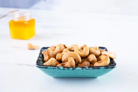 A rectangular blue bowl of whole roasted cashews stands on a white table. Photos