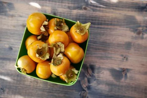 Rectangular bowl with ripe persimmons stands on a wooden table. Top view Stock Photos