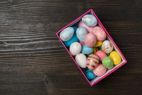 Rectangular box with bright multi-colored Easter eggs on wooden background. T Stock Photos