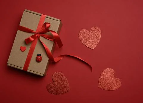 Rectangular brown cardboard box tied with a silk red ribbon on a red backgrou Stock Photos