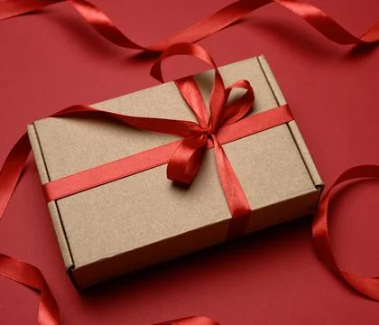Rectangular brown cardboard box tied with a silk red ribbon on a red backgrou Stock Photos