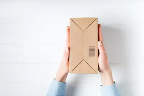 Rectangular cardboard box with barcode in female hands. Top view, white backg Stockfoto's