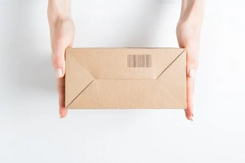 Rectangular cardboard box with barcode in female hands. Top view, white backg 스톡 사진