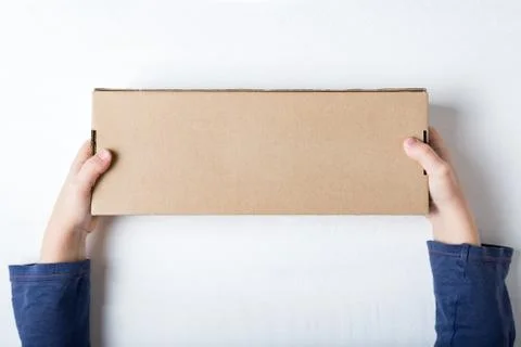 Rectangular cardboard box in children's hands. Top view, white background 스톡 사진