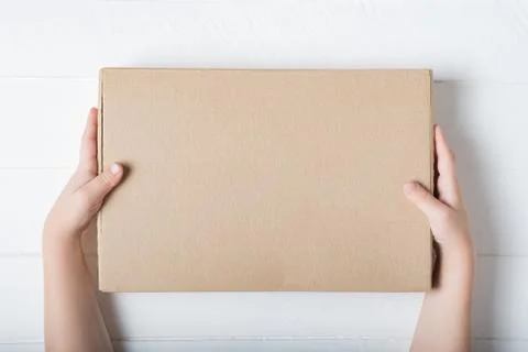Rectangular cardboard box in children's hands. Top view, white background Stockfoto's