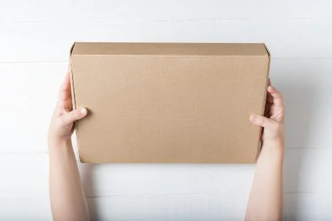 Rectangular cardboard box in children's hands. Top view, white background Stockfoto's