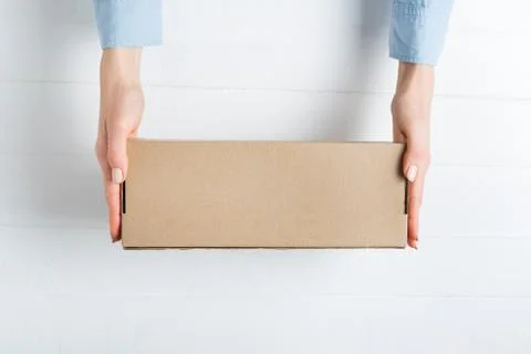 Rectangular cardboard box in female hands. Top view, white background Foto stock