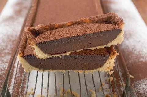 Rectangular chocolate tart with cocoa powder, partly sliced Stock Photos
