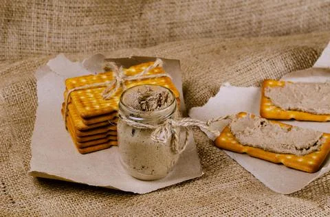 Rectangular crackers and a glass jar of liver pate on sackcloth. Close-up of  Stock Photos