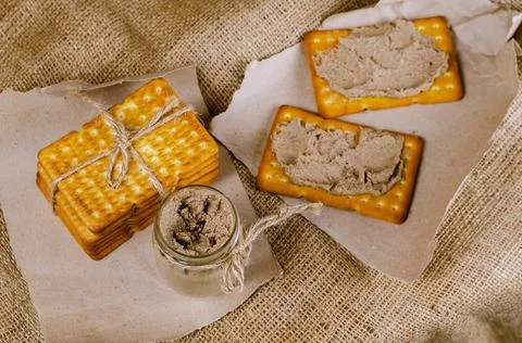 Rectangular crackers and a glass jar of liver pate on sackcloth. Stock Photos