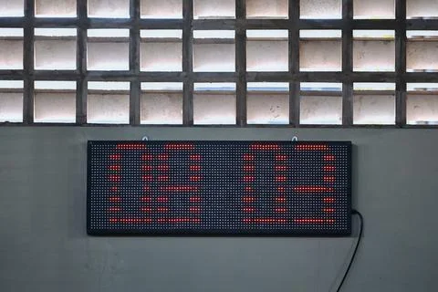 Rectangular digital LED display board mounted on a grey wall, showing red d.. Stock Photos