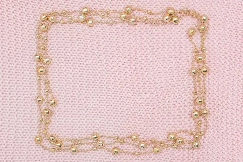 Rectangular frame from golden beads garland on knitted pink background. Top v Stock Photos