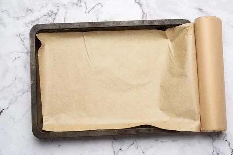 Rectangular metal baking sheet and roll of brown parchment paper on white bac Stockfoto's