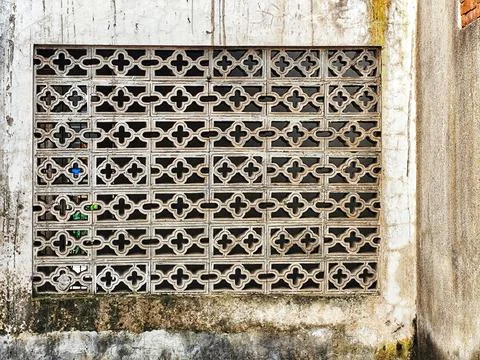 A rectangular metal vent with repeating geometric cross patterns set into a w Stock Photos