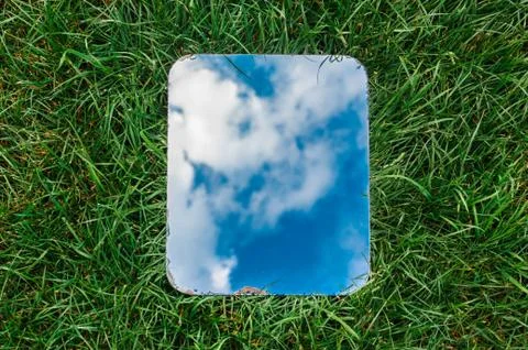 Rectangular mirror reflecting the blue sky with clouds lying on the green grass Stock Photos