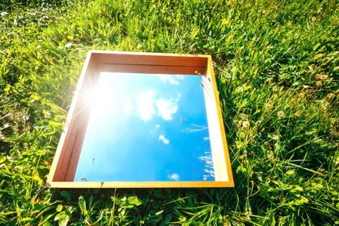 Rectangular mirror reflecting the blue sky with clouds lying on the green grass Stock Photos