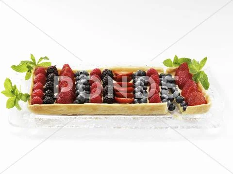 A Rectangular Mixed Berry Fruit Tart on a Glass Tray Garnished with Mint Leaves Stock Photos