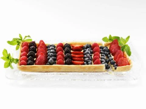 A Rectangular Mixed Berry Fruit Tart on a Glass Tray Garnished with Mint Leaves Foto stock
