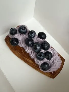 A rectangular pastry topped with light purple cream and fresh blueberries Stock Photos