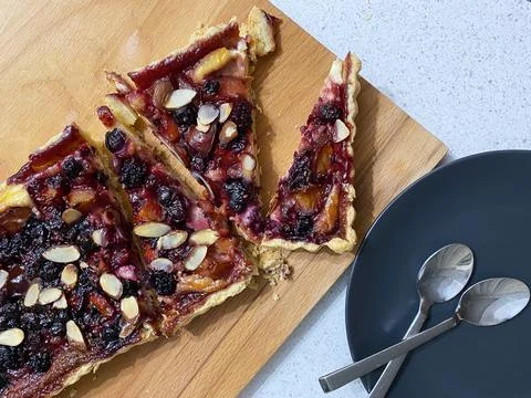 Rectangular pie with summer fruits and berries, sliced in portions, on a wooden Foto stock