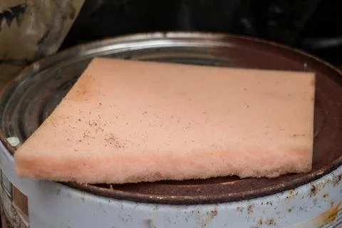A rectangular piece of pink foam sponge resting on a rusted metal paint can lid Foto stock
