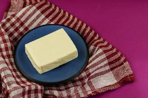 Rectangular piece of processed cheese in a blue saucer on a pink background. Foto stock