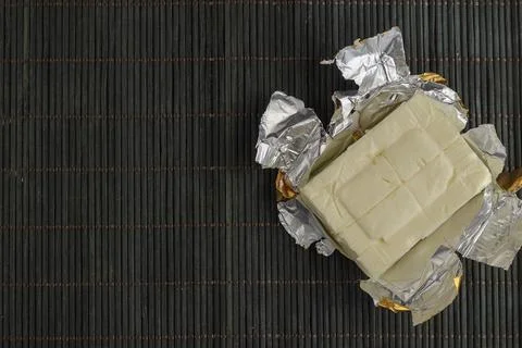 Rectangular piece of processed cheese in open foil package on a dark bamboo b Stock Photos