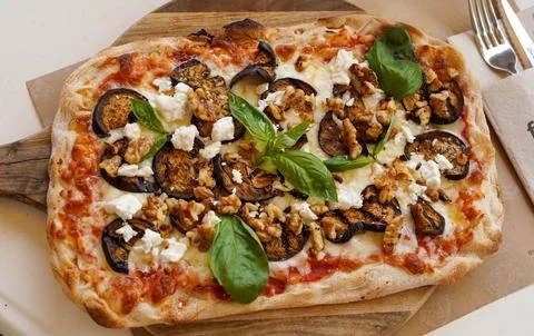 Rectangular pizza with eggplant, walnuts, and feta cheese on a wooden board Foto stock