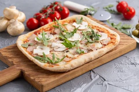  Rectangular pizza with mushrooms, tomatoes and arugula on a wooden cuttin... 스톡 사진