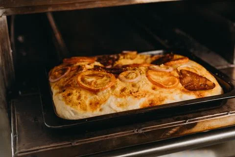 Rectangular pizza with onions, tomatoes and meat on a pan Stockfoto's
