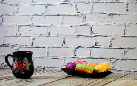 A rectangular plate with five multi-colored donuts and a black ceramic coffee Stock Photos