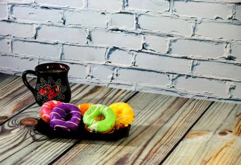 A rectangular plate with five multi-colored donuts and a black ceramic coffee Stock Photos