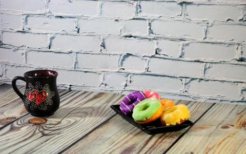 A rectangular plate with five multi-colored donuts and a black ceramic coffee Stock Photos