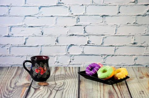 A rectangular plate with five multi-colored donuts and a black ceramic coffee Stock Photos