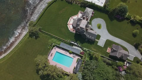 Rectangular pool sits beside turreted mansion and tennis court on coastal Stock Footage 341566290