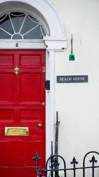 A rectangular sign next to a red front door with Beach House near Tenby harbour 스톡 사진