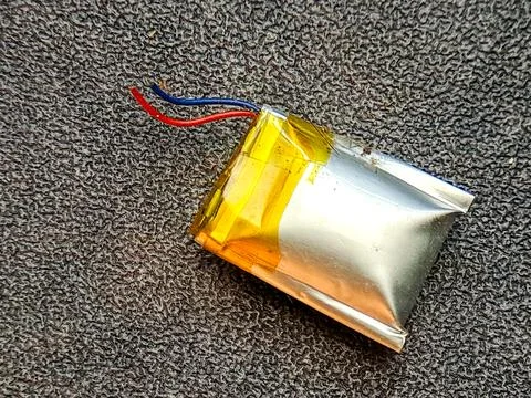 A rectangular silver battery pack with red and blue wires sits on grey text.. Stock Photos