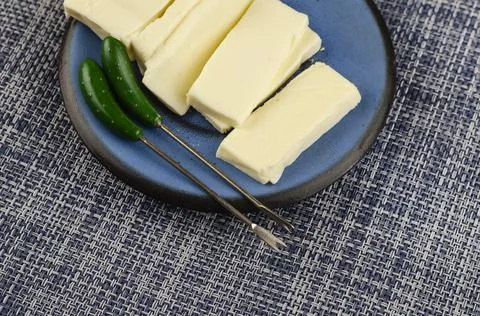Rectangular slice of processed cheese in a blue saucer on a denim background. Stock Photos