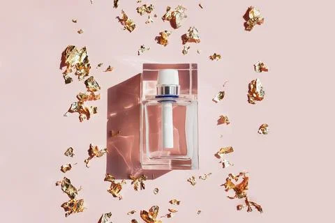 Rectangular transparent glass perfume bottle, pieces of golden paper on pink Stock Photos