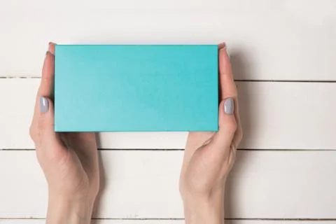 Rectangular turquoise box in female hands. Top view. White table on the backg Stock Photos
