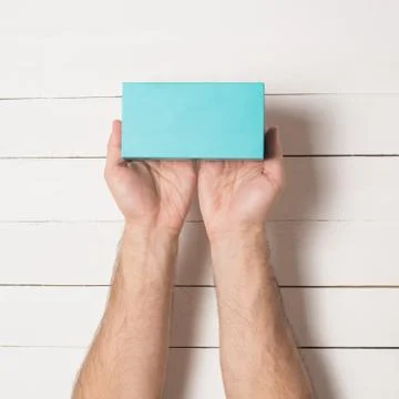 Rectangular turquoise box in male hands. Top view. White table on the backgro 스톡 사진