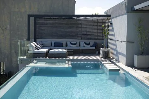 Rectangular turquoise pool is rippling on rooftop deck, with rattan sectional Photos