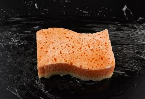 Rectangular wet orange washcloth with white foam on a black background 스톡 사진