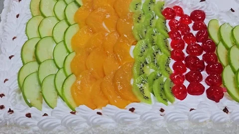 A rectangular white cream cake topped with rows of colorful fresh fruit slices, 스톡 동영상 321700355