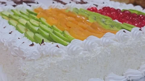 A rectangular white cream cake topped with rows of colorful fresh fruit slices 스톡 동영상 321701037