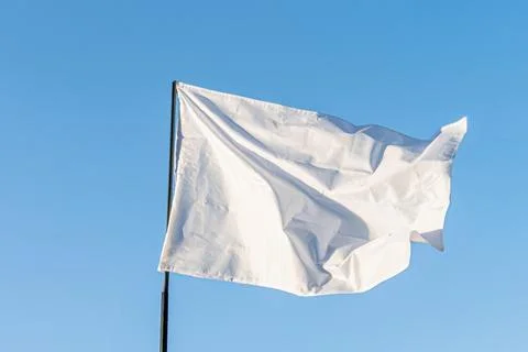 A rectangular, white flag with fringed edge fluttering against a clear blue s Stock Photos