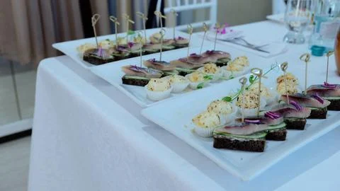 Rectangular white plates showcasing herring canapes, cucumber slices, rye bread Stock Photos