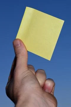 Rectangular yellow note paper held by one hand raising up to the sky. A person 스톡 사진