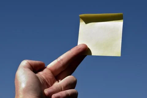 Rectangular yellow note paper held by one hand raising up to the sky. A person 스톡 사진